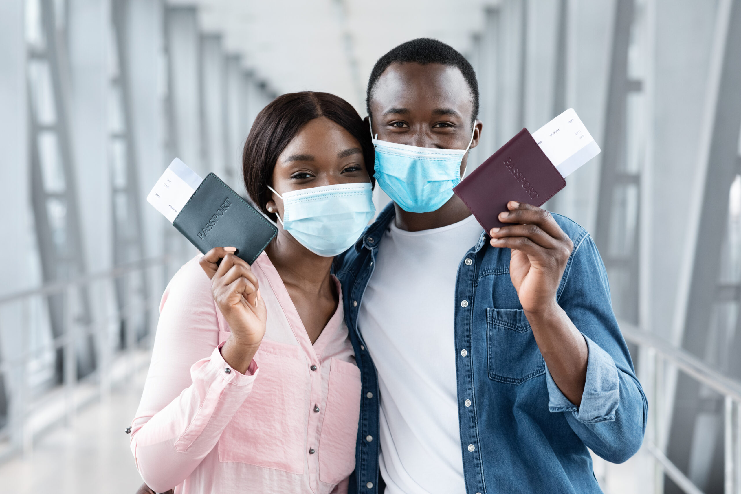 Travel Safe During Coronavirus Pandemic. Black couple in protective medical masks posing with passports and tickets at airport, closeup